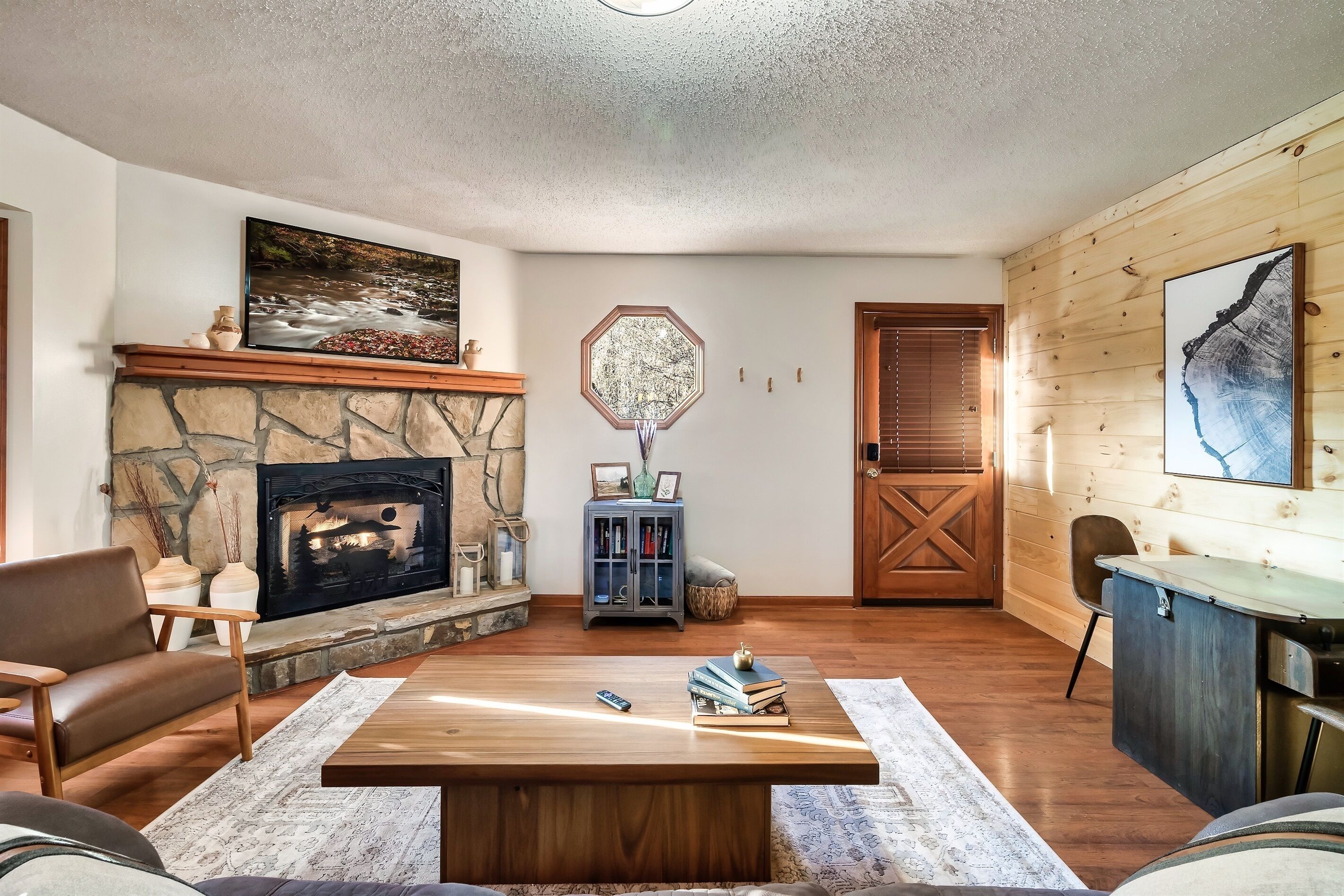 Un salón con chimenea de piedra, una mesa de centro de madera, una estantería y un cuadro grande en la pared.