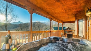 A hot tub on a wooden deck with a view of mountains and a house in the background. - Gatlinburg Mountain View Cabin | Hot Tub & Arcade (Gatlinburg)