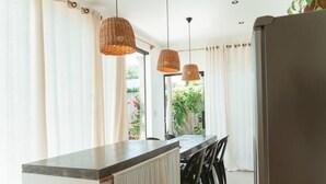 A modern kitchen with a central island, pendant lights, and a view of greenery outside. - Comfortable and charming house 360m from the beach, Porto Seguro. (Porto Seguro)
