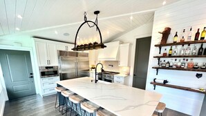A modern kitchen with a large island, bar stools, stainless steel appliances, and a wine rack. - Lakefront(partial) dock pool hot tub barrel rolled sauna gym bunk house fire pit (Shawnigan Lake)