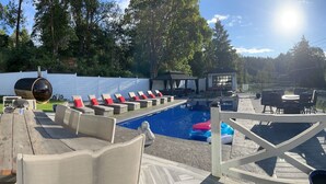 A pool area with lounge chairs, a barbecue, and a view of a lake and forest. - Lakefront(partial) dock pool hot tub barrel rolled sauna gym bunk house fire pit (Shawnigan Lake)