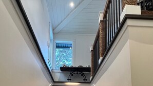 A staircase with built-in lighting, leading to a landing with a window and a small table. - Lakefront(partial) dock pool hot tub barrel rolled sauna gym bunk house fire pit (Shawnigan Lake)
