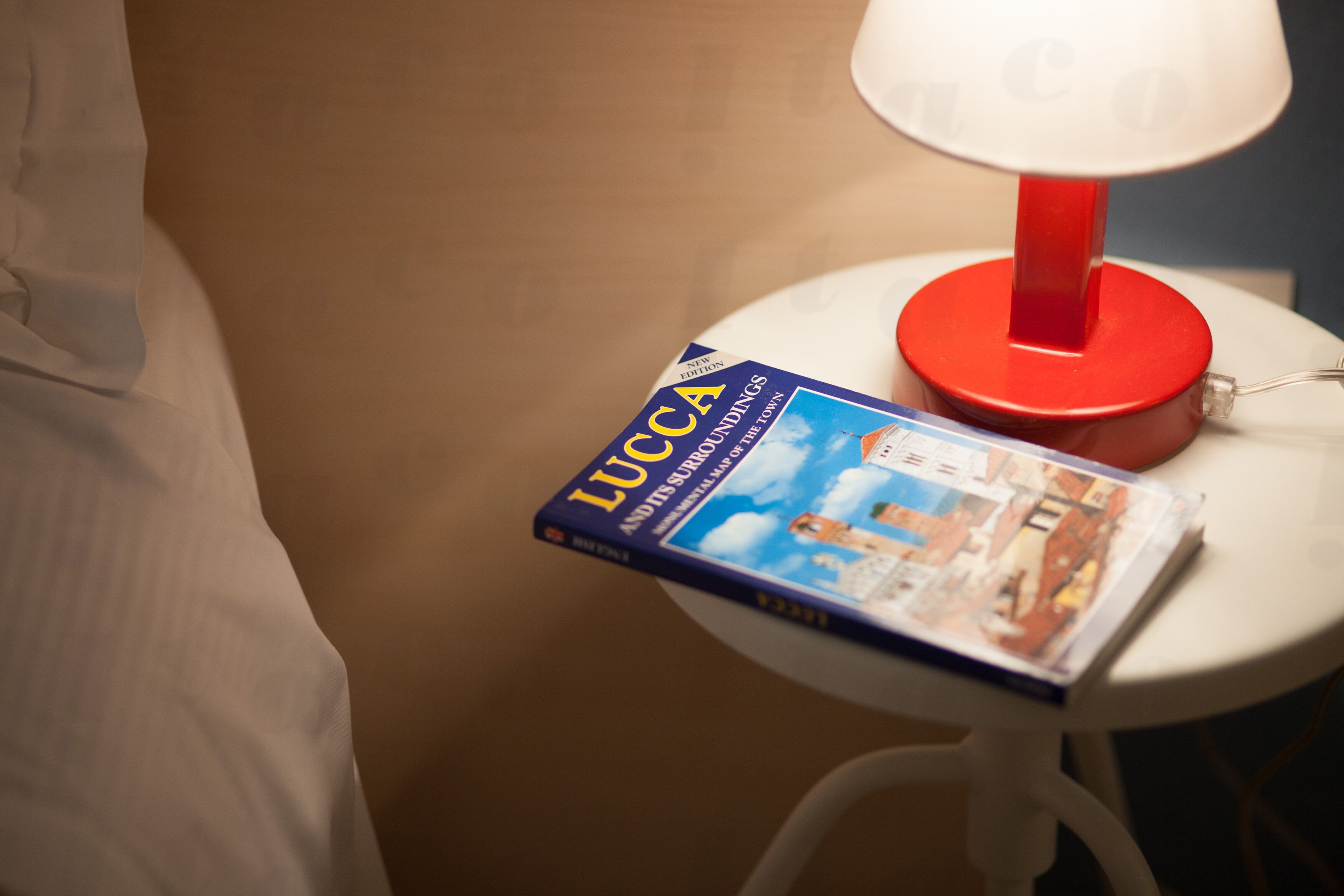 A book titled 'LUCCA' on a white table next to a red lamp.