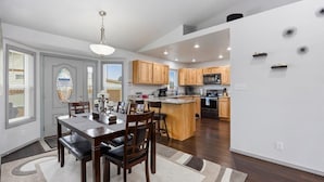 A modern kitchen with wooden cabinets, a central island, and a dining area with a table and chairs.