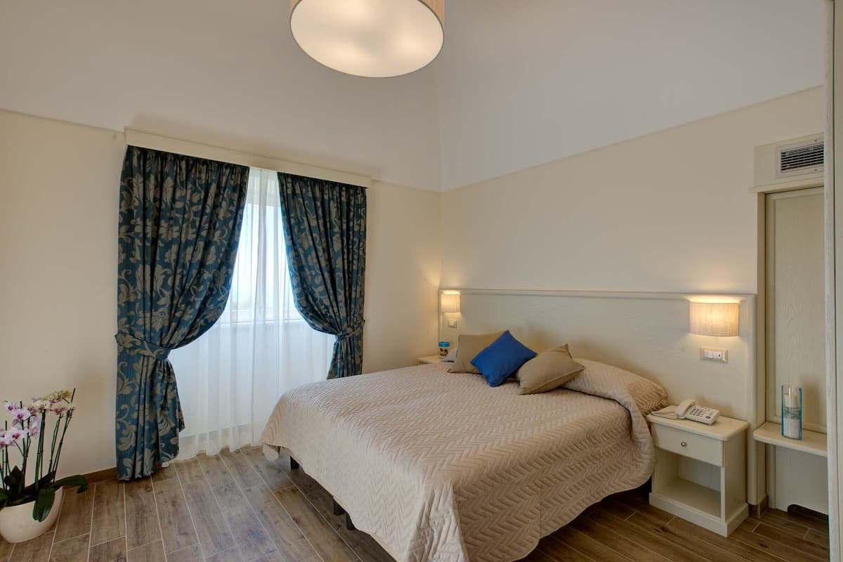 Un dormitorio con cama, mesitas de noche, lámpara y planta en maceta.