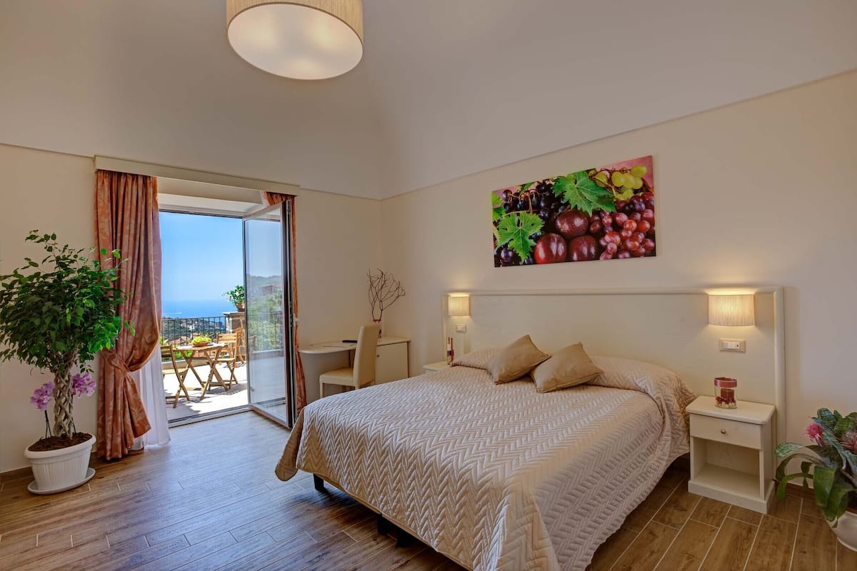 Un dormitorio con una cama, un escritorio, una silla, una planta en maceta y un cuadro de uvas en la pared.