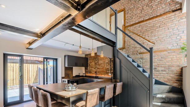 A modern kitchen with a central island, bar stools, and a staircase with exposed brick walls. - The Warren - UK42858 (Skirlaugh)