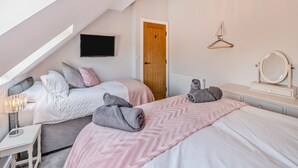 A bedroom with two beds, a TV, a wooden door, a vanity with a mirror, and a chandelier. - The Warren - UK42858 (Skirlaugh)