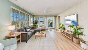 A spacious living room with a large flat-screen TV, a sectional sofa, a coffee table, and a view through the sliding glass doors. - Ocean & Sound Views, Game Room, Steps to Beach! (Surf City)