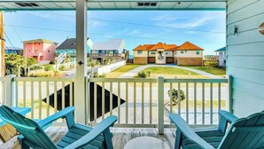 A covered porch with blue chairs and a table, overlooking a residential area with houses and a clear sky. - Ocean & Sound Views, Game Room, Steps to Beach! (Surf City)