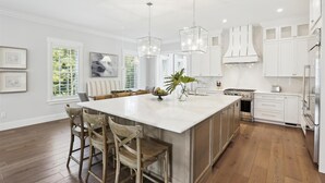 Una cocina moderna con una isla grande, taburetes de bar de madera, iluminación colgante y alacenas blancas.