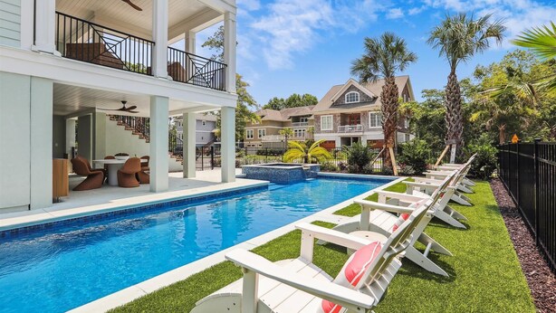 Zona de piscina con sillones de descanso, un área de estar cubierta y vista a un edificio residencial al fondo.
