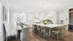 Una cocina moderna con armarios blancos, una isla central con taburetes e iluminación colgante.