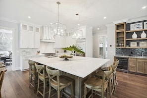 A spacious kitchen with a large island, white cabinetry, and a modern chandelier.