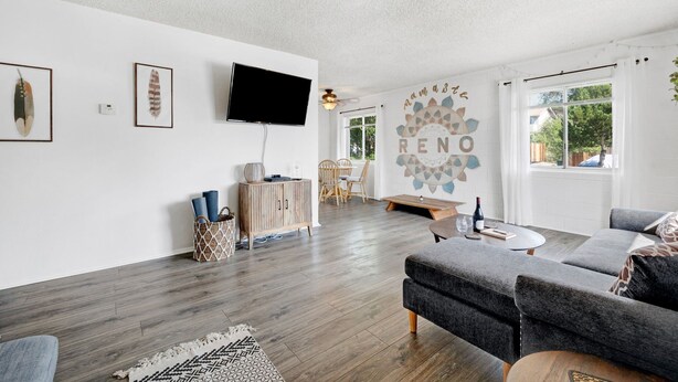 Un salon moderne avec un canapé gris, un plancher en bois, un téléviseur à écran plat et une fresque murale sur laquelle est inscrit le mot « RENO ».