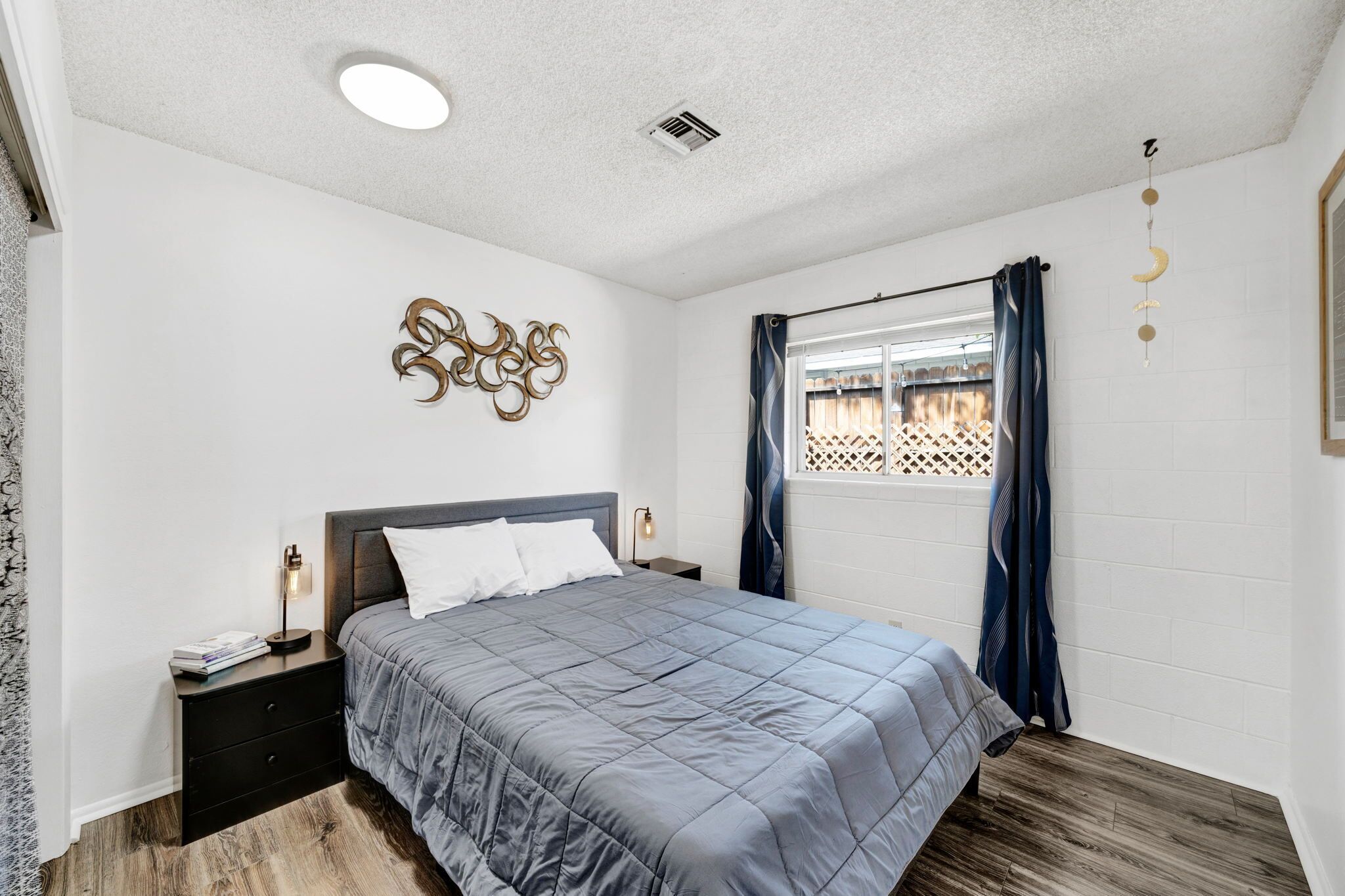 A bedroom with a bed, nightstands, a wall decor piece, a window with curtains, and a ceiling light.