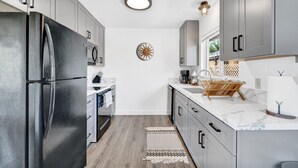 Une cuisine moderne avec des meubles gris, un réfrigérateur noir, un plan de travail en marbre et un plancher en bois.