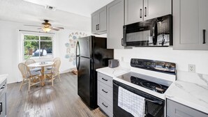 Une cuisine moderne avec des meubles gris, un réfrigérateur noir, un four à micro-ondes, une cuisinière et un coin repas comprenant une table et des chaises en bois.