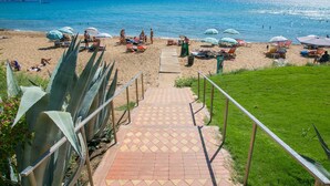 A beach with a paved walkway leading to the water, surrounded by sun loungers and umbrellas.