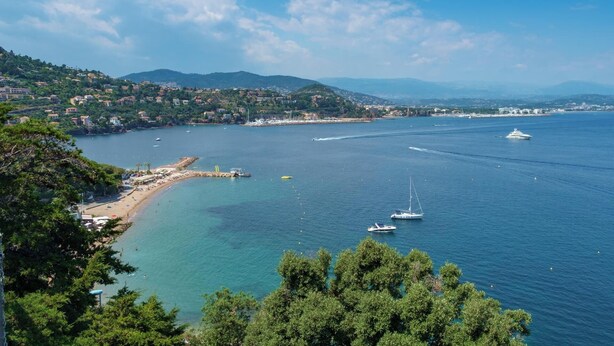 Uma vila costeira com praia, barcos e montanhas ao fundo.