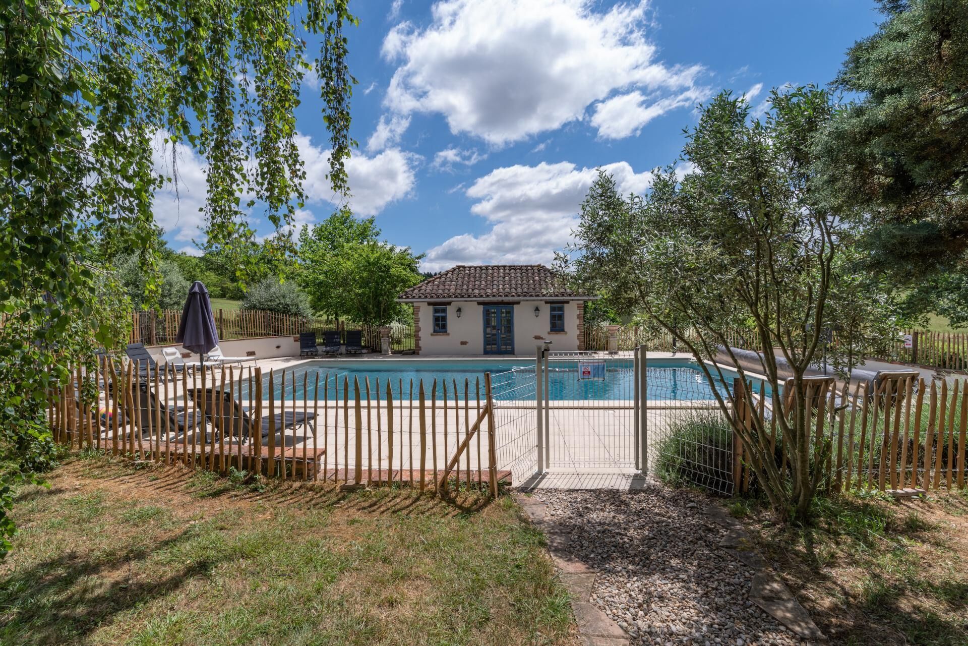 Une maison avec une piscine, entourée d’une clôture en bois et d’arbres.