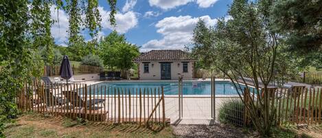 Une maison avec une piscine, entourée d’une clôture en bois et d’arbres.