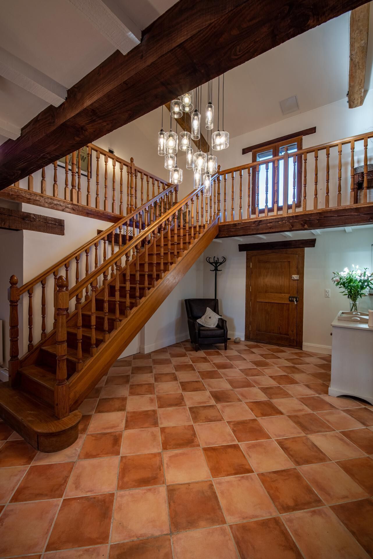 Une pièce spacieuse avec un escalier en bois, un lustre et un sol à carreaux.