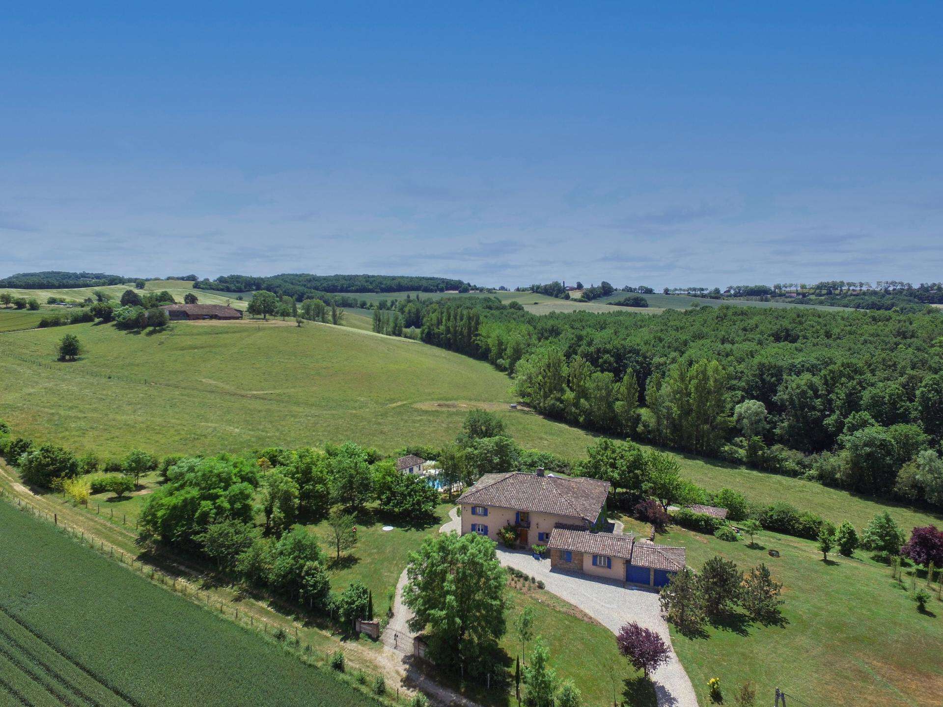 Une propriété rurale avec une grande maison entourée de champs verdoyants et d’arbres.