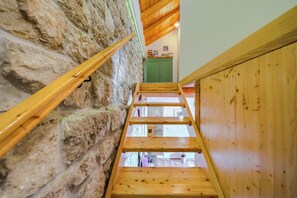 Un escalier en bois, avec un mur en pierre d’un côté et un panneau en bois de l’autre, mène à une pièce dotée d’une porte verte et d’une fenêtre.