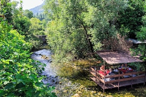 Estructura de madera rústica con una mesa y sillas, rodeada de vegetación exuberante y un río serpenteante.