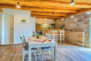 A dining area with a table set for two, a kitchen with stone walls, and a wooden ceiling.