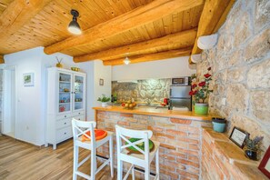 Una cocina con pared de piedra, vigas de madera en el techo, un armario blanco y dos taburetes de bar.