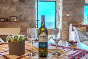 Una botella de vino Vina Palihnic, dos copas de vino vacías y un arreglo floral sobre una mesa, con una pared de piedra y una ventana al fondo.