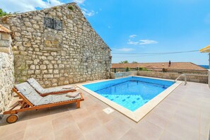 Un edificio de piedra con piscina, una silla de descanso y una terraza de baldosas.