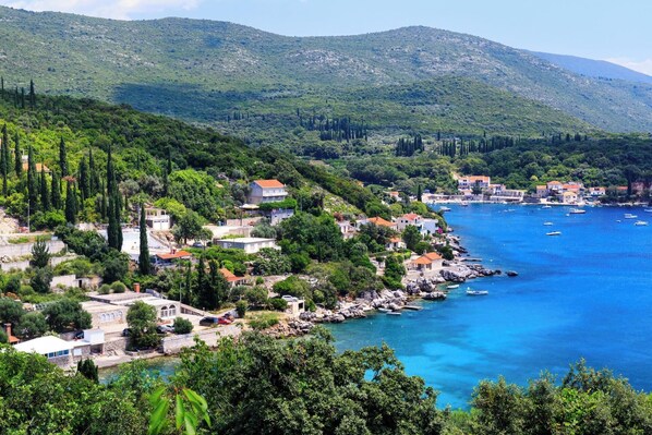 Une ville côtière avec des bâtiments qui bordent le front de mer, une mer d’un bleu limpide et des collines verdoyantes en arrière-plan.