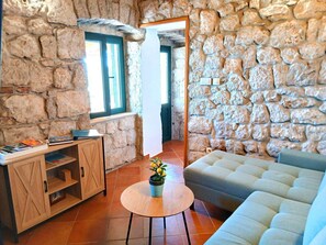 Une pièce avec un mur en pierre, un meuble en bois, une table ronde avec une plante, un canapé et une fenêtre.