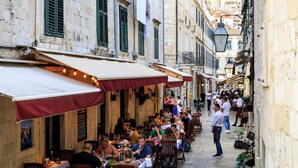 A narrow street lined with outdoor cafes, stone buildings, and a view of a hillside. - Ivana - Two Bedroom Villa, Sleeps 3 (Dubrovnik)