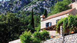 A stone building with a tiled roof, surrounded by lush greenery and a rocky mountain backdrop. - Ivana - Two Bedroom Villa, Sleeps 3 (Dubrovnik)