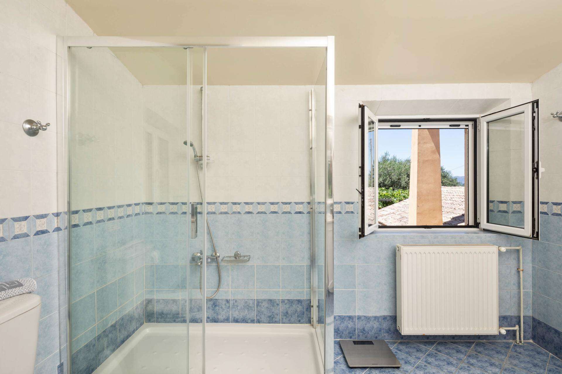Ein Badezimmer mit einer gläsernen Duschkabine, einem Fenster mit Aussicht und einer Heizung.