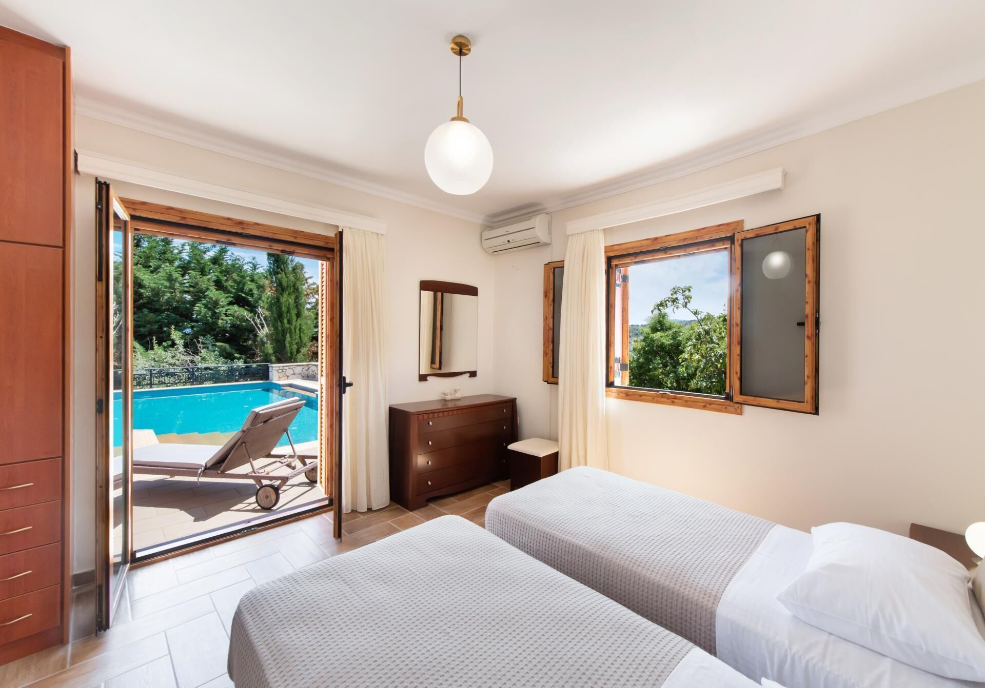 Ein Schlafzimmer mit zwei Betten, einem Schminktisch, einem Spiegel und einem Fenster mit Blick auf einen Swimmingpool.