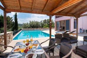A poolside dining area with a view of a pool, outdoor furniture, and a building in the background.