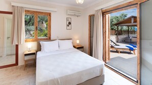 A bedroom with a bed, bedside tables, a window, and a view of an outdoor area with a pool and lounge chairs. - Pegasus - Three Bedroom Villa, Sleeps 6 (Spartochori)