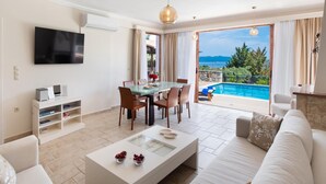 A modern living room with a glass dining table, a flat-screen TV, and a sofa. - Pegasus - Three Bedroom Villa, Sleeps 6 (Spartochori)