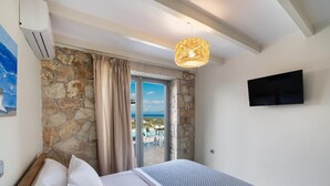 Ein Schlafzimmer mit Steinsturz, einem Bett mit weißen Leinen, einem Deckenventilator und einem an der Wand montierten Fernseher.