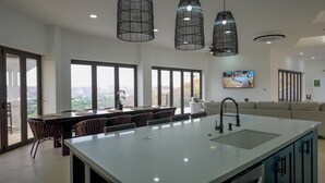 Una cocina moderna con una isla grande, luces colgantes y vistas al exterior a través de amplios ventanales.