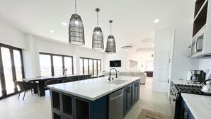 Una cocina moderna con una isla central, iluminación colgante y un amplio ventanal que proporciona luz natural.