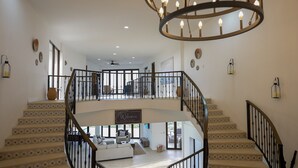 Un interior espacioso con una imponente escalera, un candelabro y un cartel de bienvenida.