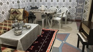 Un comedor con una mesa dispuesta para cuatro personas, rodeada de sillas blancas, un papel tapiz con diseño y un televisor a la derecha.