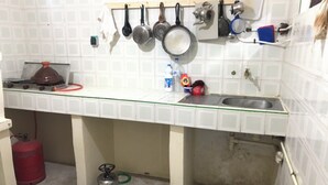Una cocina con paredes de azulejos blancos, una estufa a gas, un lavamanos y diversos utensilios de cocina colgados en la pared.