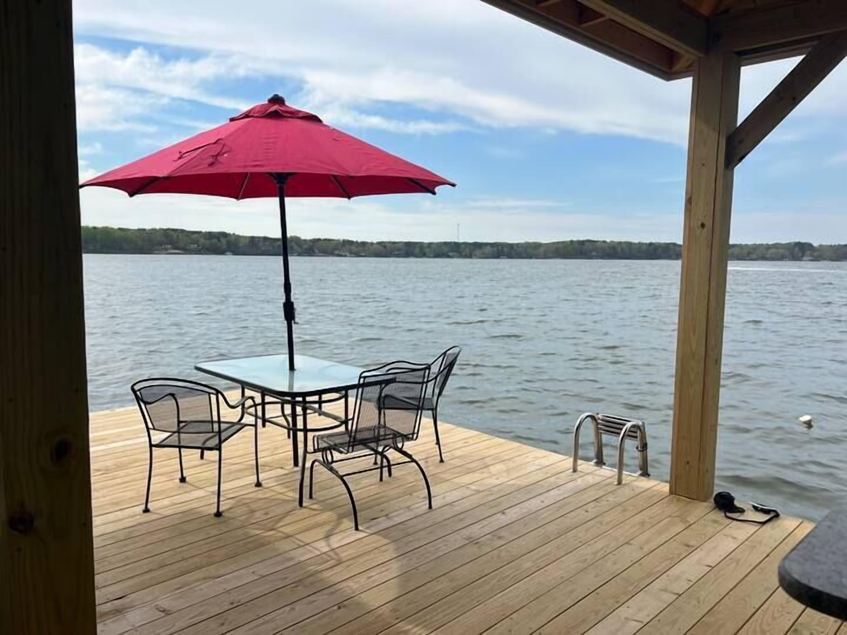 Une terrasse en bois avec une table et des chaises, un parasol rouge et une vue sur un lac.